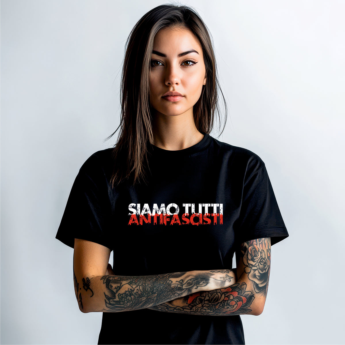 „Person mit langen dunklen Haaren trägt schwarzes T‑Shirt mit Frontprint ‚SIAMO TUTTI ANTIFASCISTI‘ in Weiß und Rot, sichtbare Tattoos an beiden Unterarmen – klares antifaschistisches Statement vor hellem Hintergrund.“