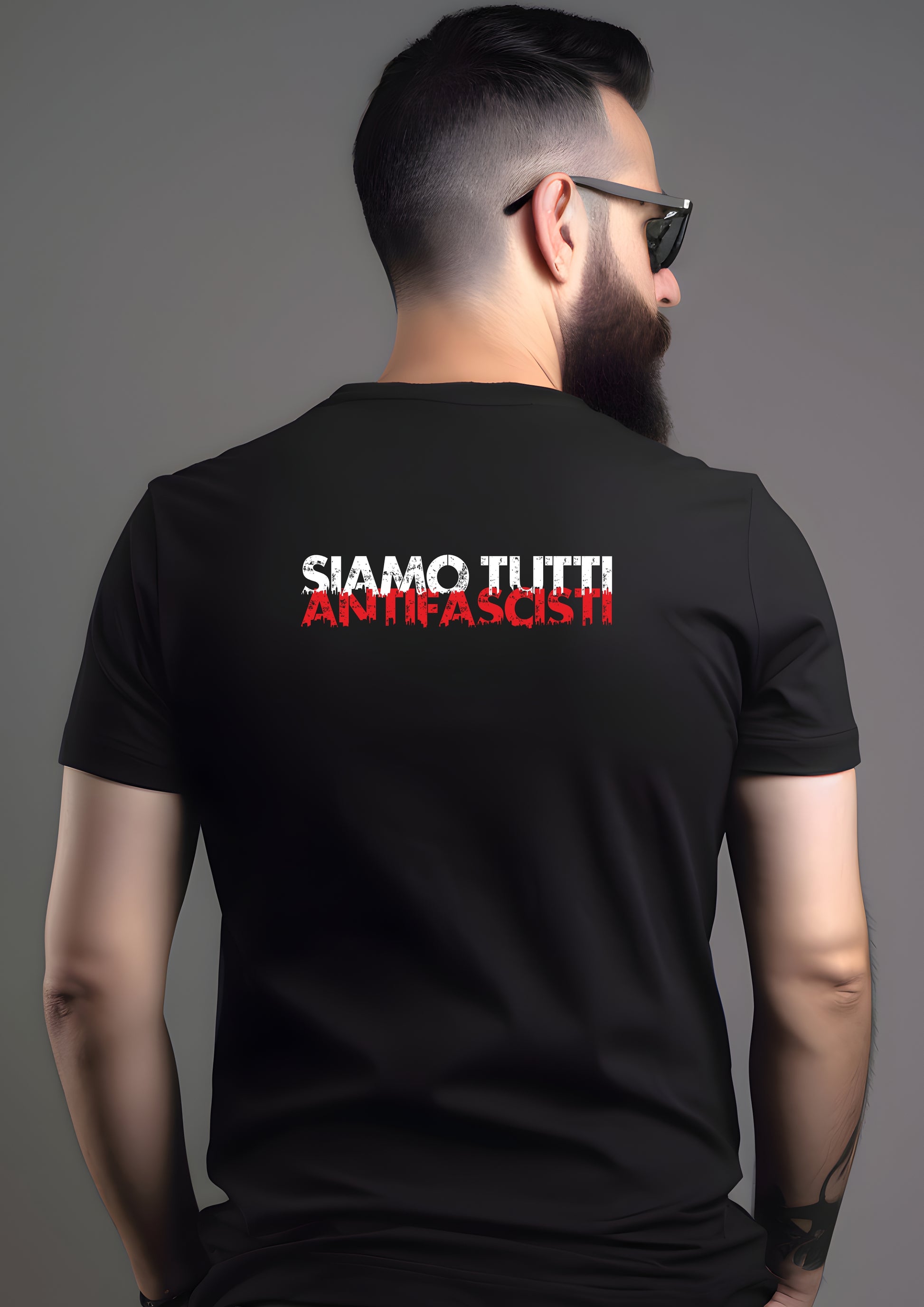Person mit Bart und Sonnenbrille trägt ein schwarzes T-Shirt mit dem Statement „SIAMO TUTTI ANTIFASCISTI“ in weiß-roter, distressed Schrift auf dem Rücken.