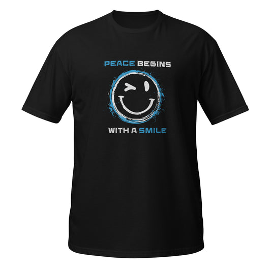 Schwarzes Unisex T‑Shirt mit großem gelbem Smiley, der zwinkert, umgeben von einem blauen, grob gemalten Kreis. Darüber und darunter steht in weiß‑blauer Schrift „Peace Begins With a Smile“.